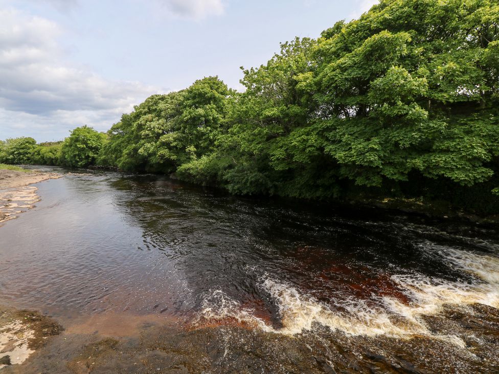 A river with trees along the bank and cloudy sky at Doonalton House in Dromore West, County Sligo