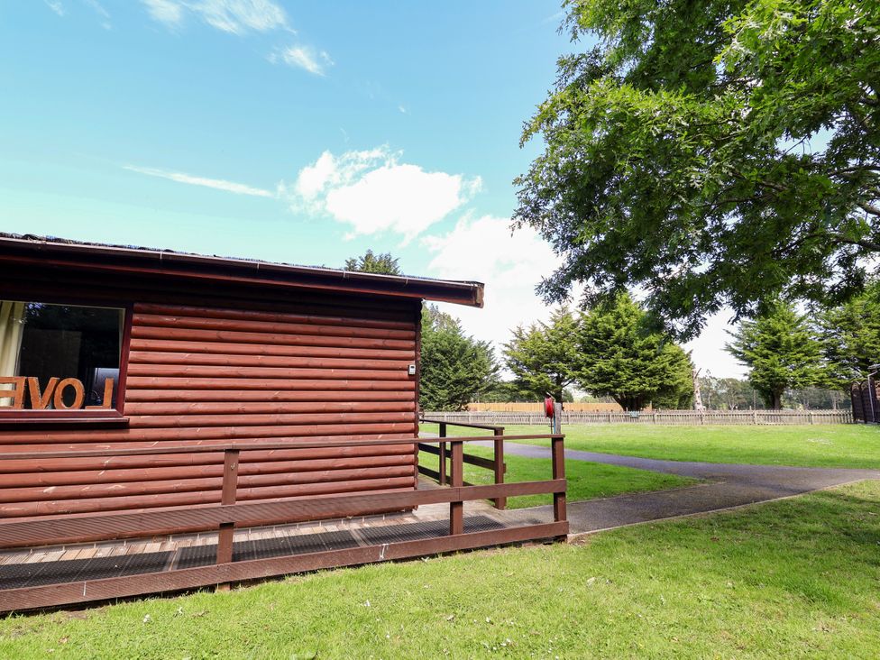 A wooden cabin with a deck and grass area at The Red in Llanerch Park near St Asaph