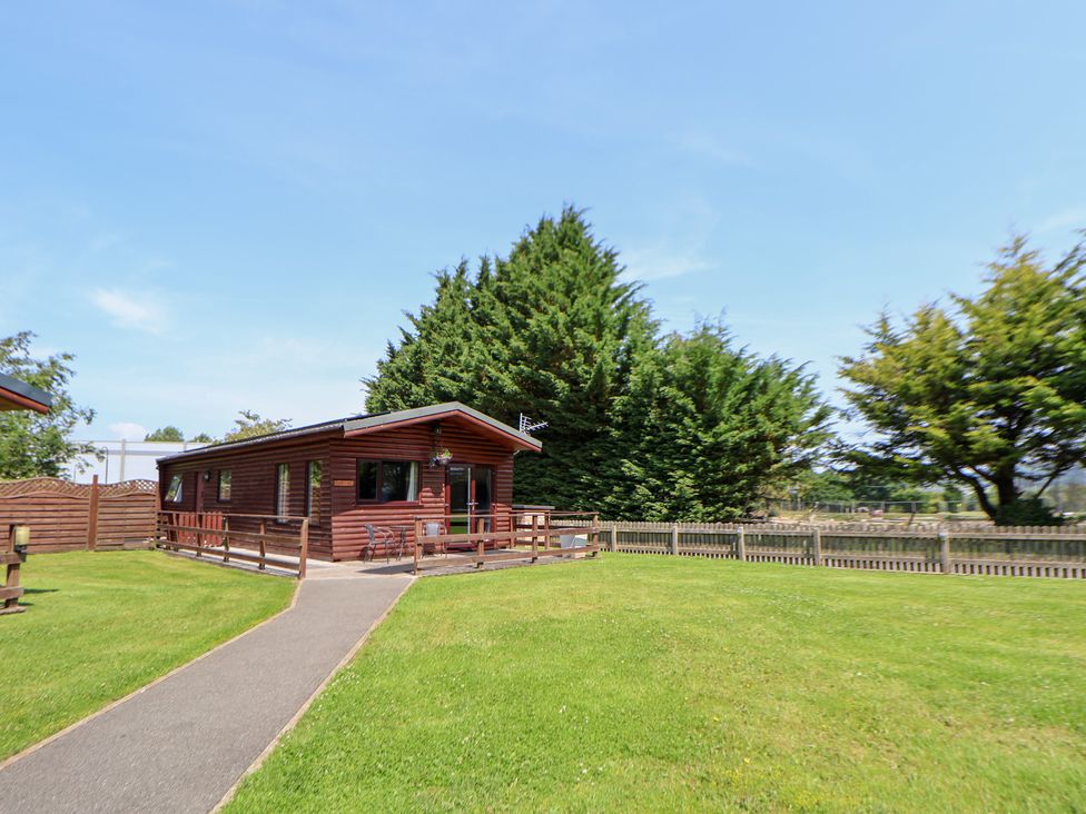 An outdoor view of a log cabin with grass and trees at The Fallows near Llanerch Park near St Asaph