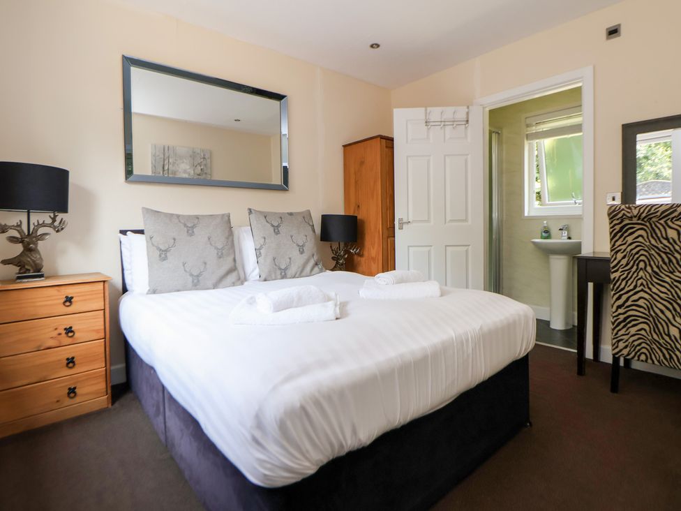A bedroom with a bed, mirror, lamp, and ensuite bathroom at The Fallows in Llanerch Park near St Asaph