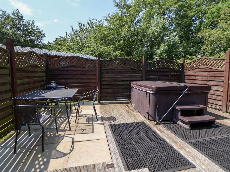 An outdoor area with a hot tub and a table with chairs at The Fallows in Llanerch Park near St Asaph
