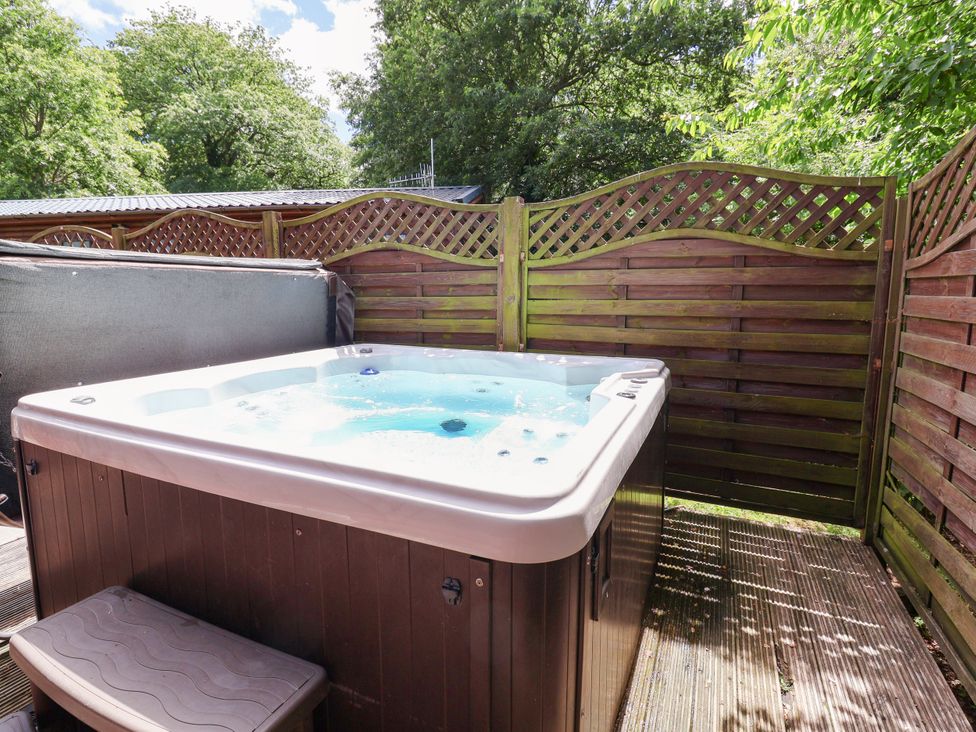 A hot tub on a deck surrounded by a privacy screen at The Roe in Llanerch Park near St Asaph