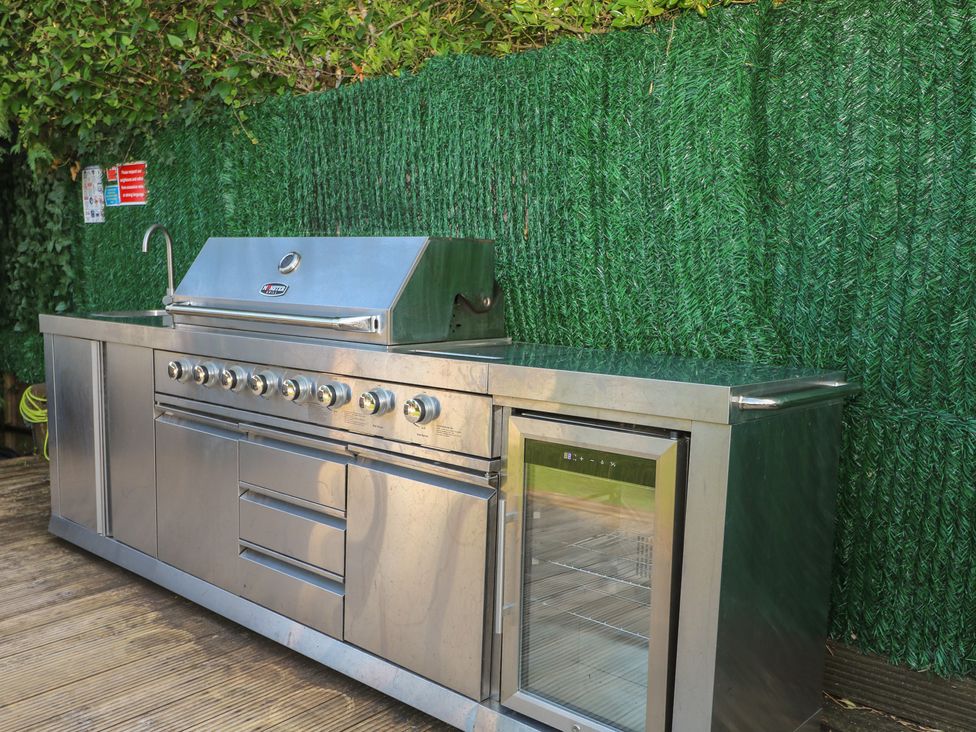 An outdoor kitchen with a grill, fridge, and sink at Coventina, Wraysbury