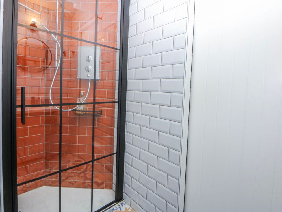 A shower with glass doors and tiled walls at East meets West Criccieth