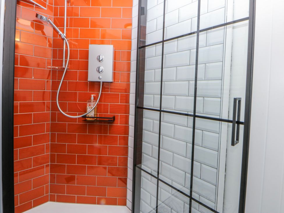A shower with red tiles and a glass door at East meets West Criccieth