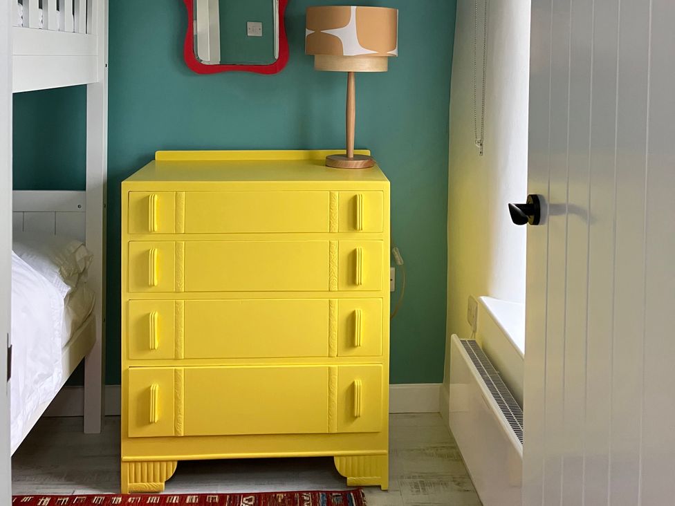 A yellow dresser and lamp in a bedroom at East meets West Criccieth