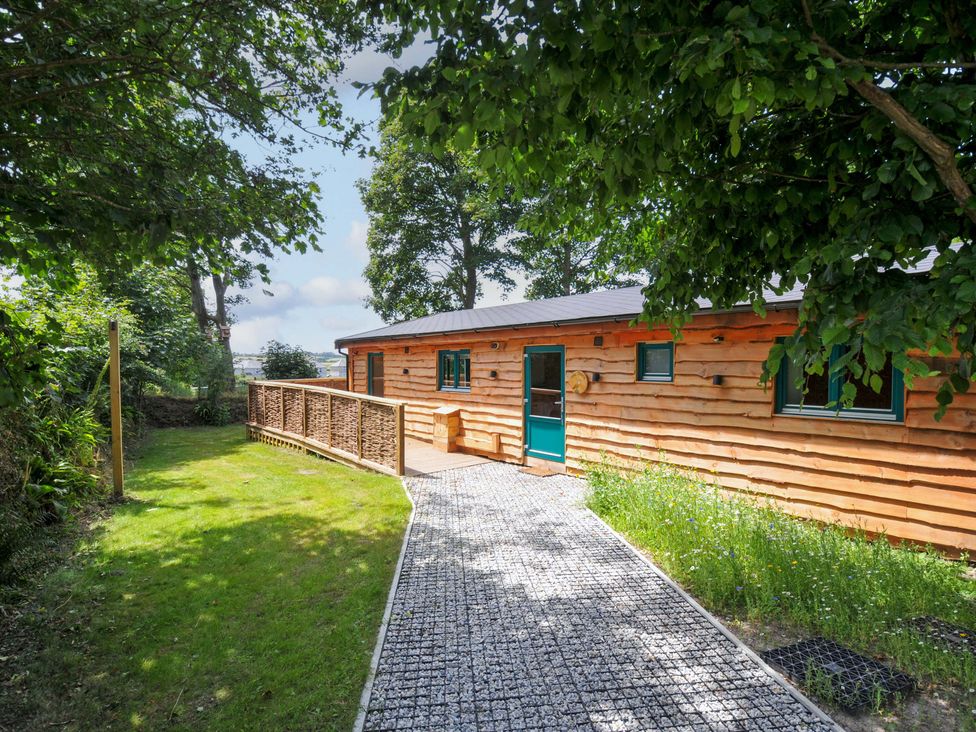 A cabin with a pathway leading to a door surrounded by grass and trees at Owl Lodge Menheniot