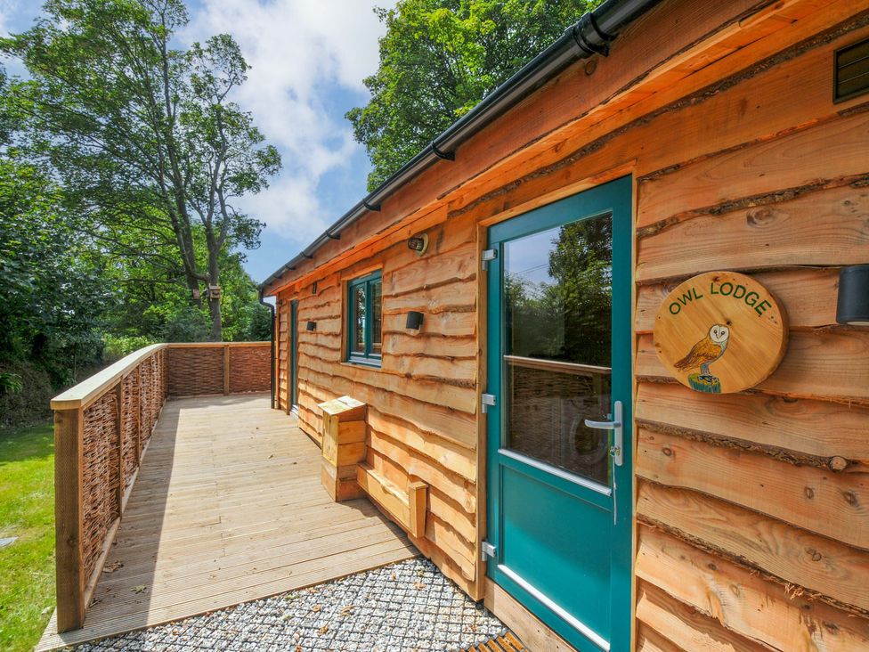 A wooden lodge with a deck and sign at Owl Lodge in Menheniot