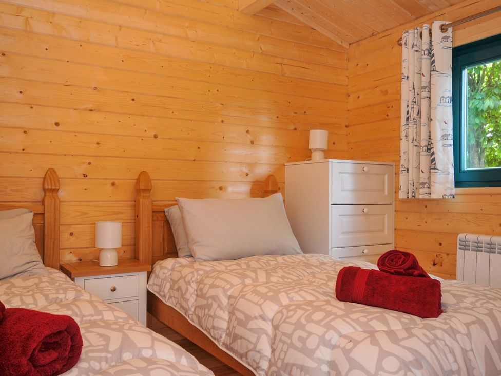 A bedroom with two beds, a lamp, and a drawer at Owl Lodge in Menheniot