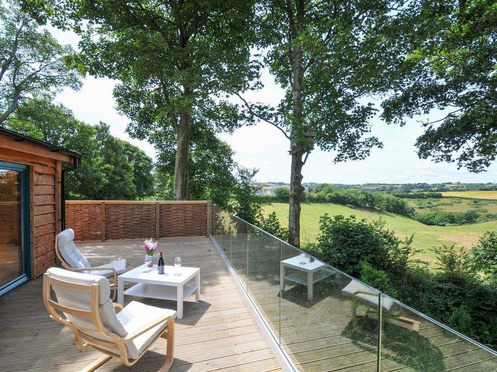 A deck with chairs and a table overlooking fields at Owl Lodge in Menheniot