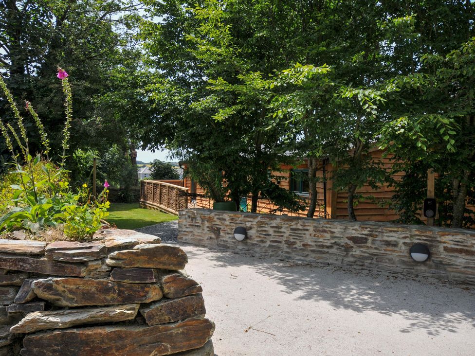 An outdoor area with a stone wall and wooden structure at Owl Lodge in Menheniot