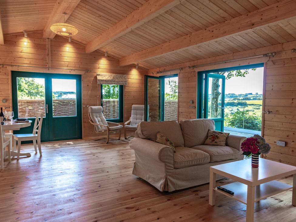 A living room with windows and a table at Owl Lodge in Menheniot