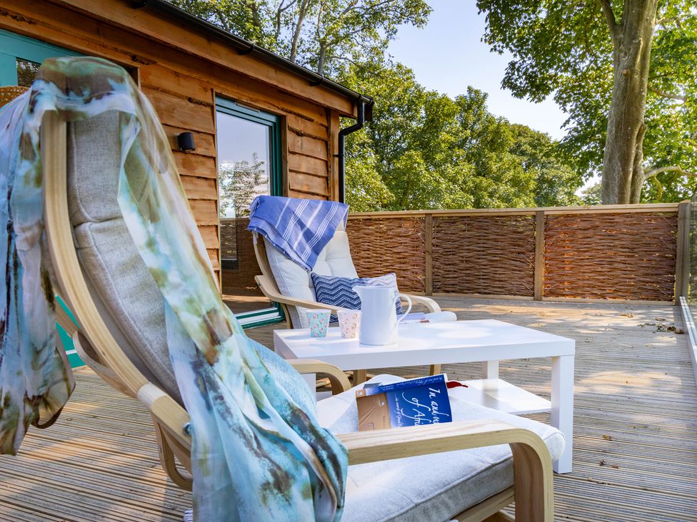 A deck with chairs, table, and a book at Owl Lodge in Menheniot