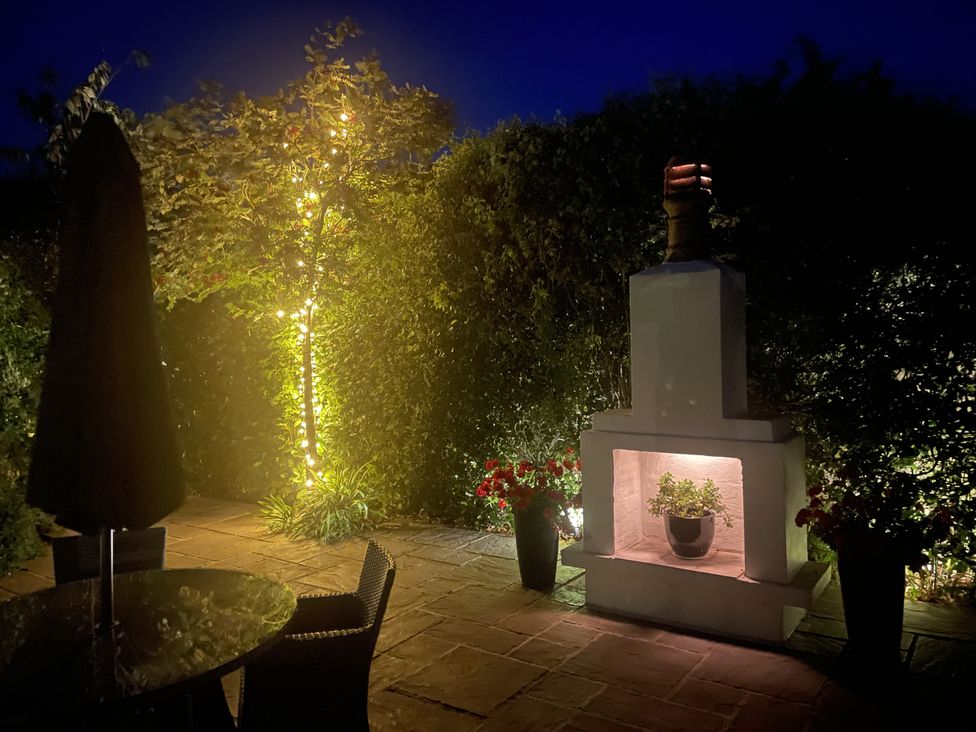 A garden with a table, umbrella, and a fireplace with a plant at No 8, Burnham-On-Sea