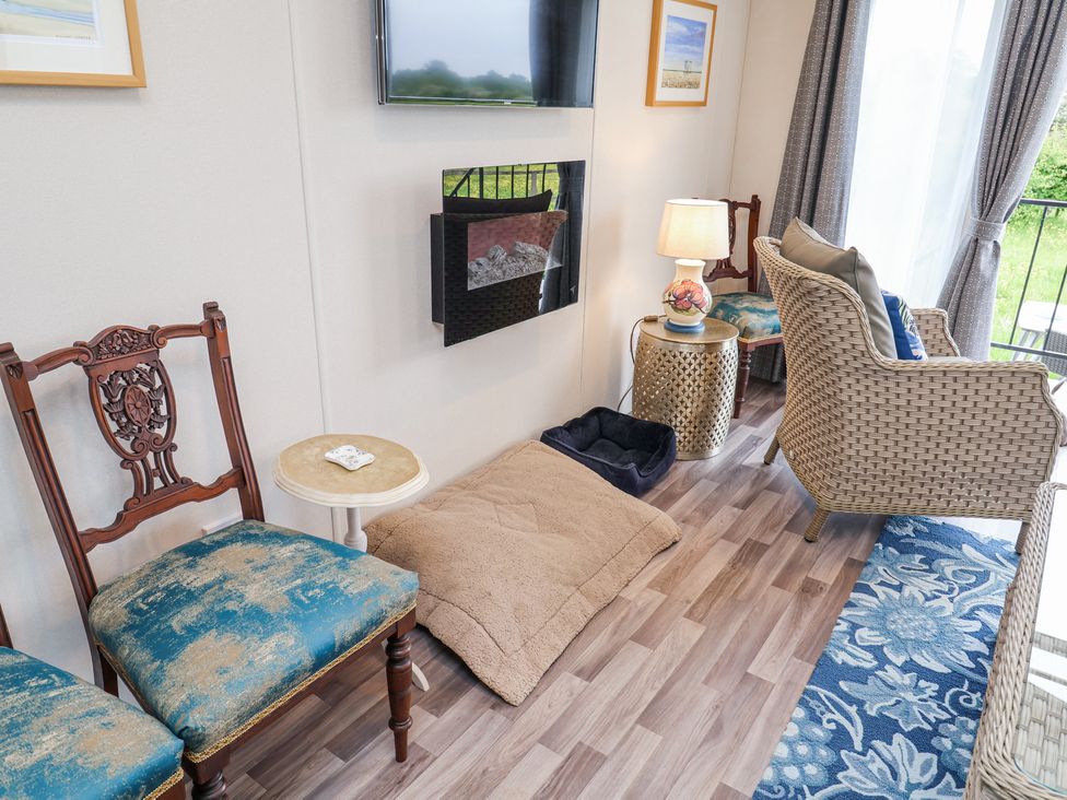 A sitting area with antique wooden chairs a woven armchair small side tables lamps a wall mounted tv and fireplace and pet beds at The Hoot in Great Finborough near Stowmarket