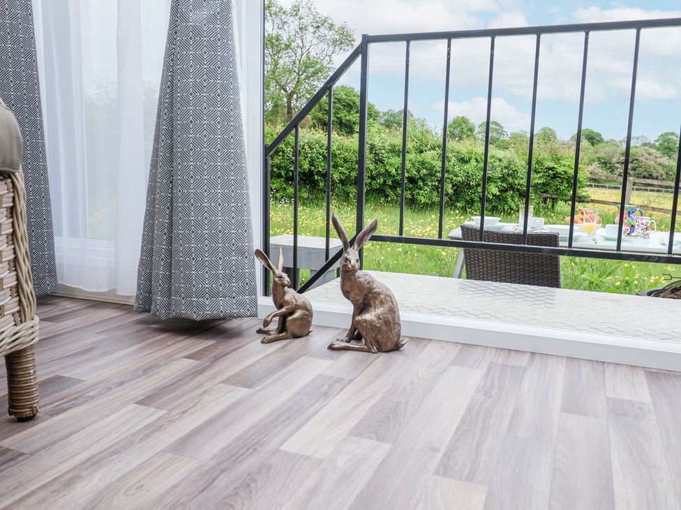 Two rabbit sculptures on a wooden floor next to a glass door with gray patterned curtains and an outdoor patio with a table and chairs at The Hoot in Great Finborough near Stowmarket