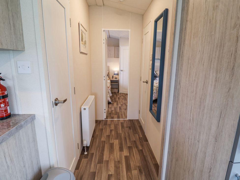 A hallway with wood flooring a radiator a wall mirror and doors leading to other rooms at The Hoot in Great Finborough near Stowmarket