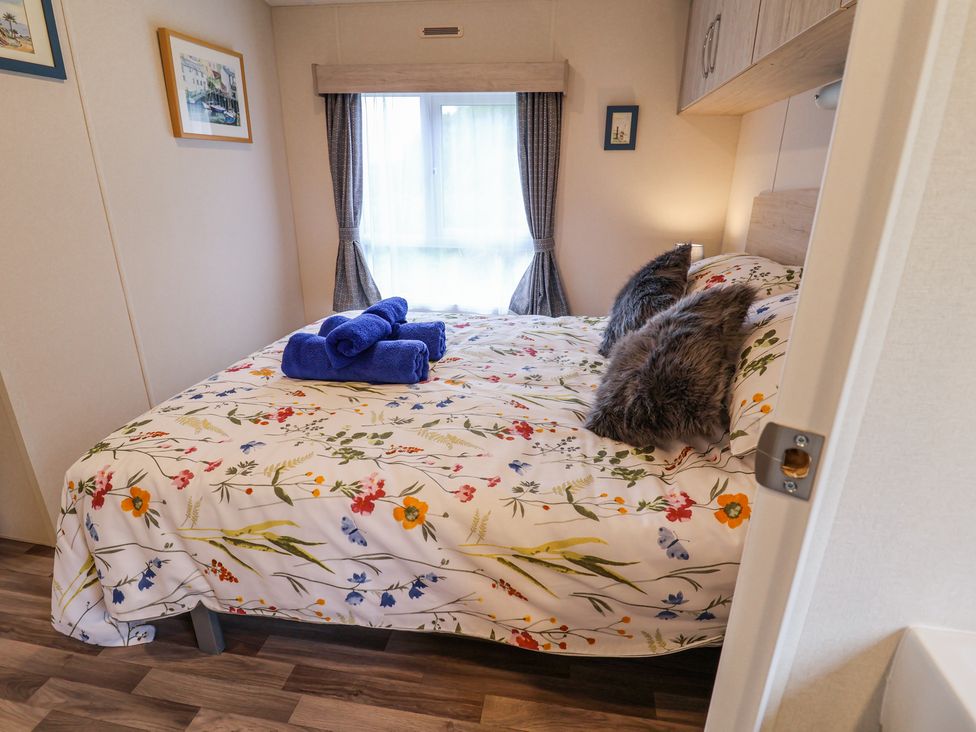 A bedroom with a bed with floral bedding and blue towels on it by a window with curtains at The Hoot in Great Finborough near Stowmarket