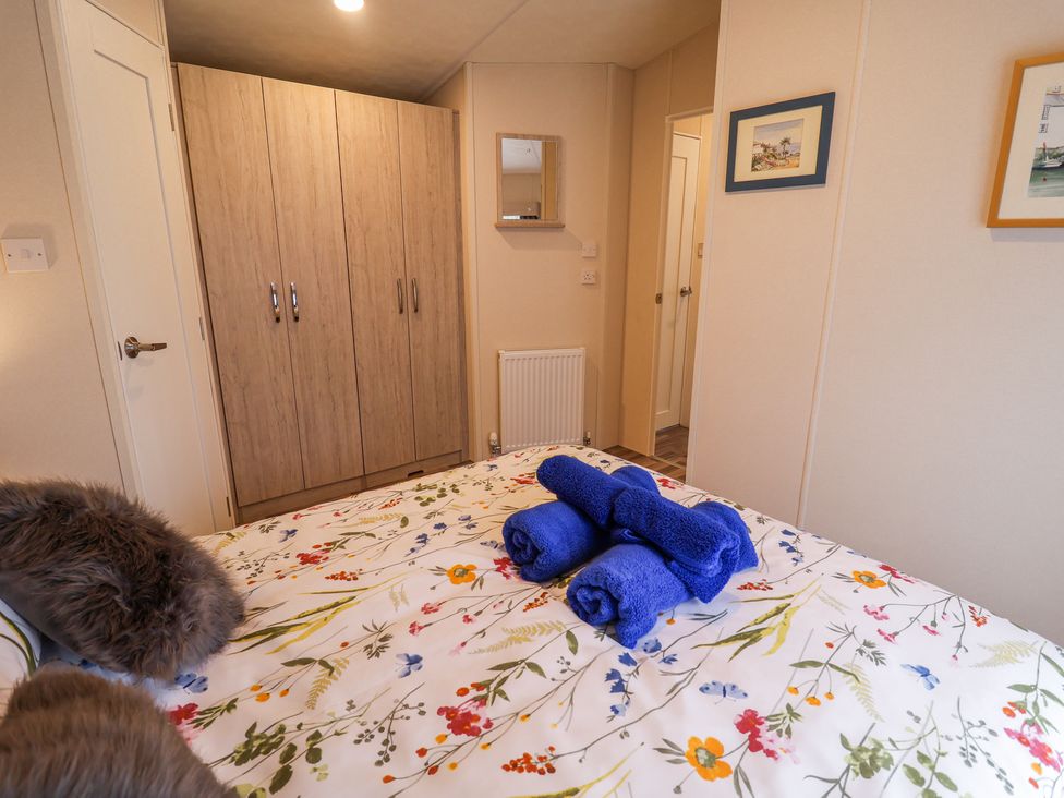A bedroom with a floral bedspread and folded blue towels on the bed and a wooden wardrobe against the wall at The Hoot Great Finborough near Stowmarket