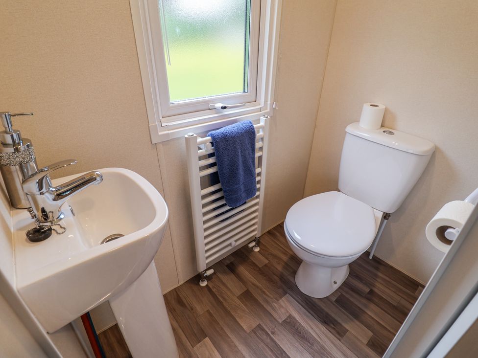 A small bathroom with a white toilet and sink a blue hand towel on a radiator under a frosted window at The Hoot in Great Finborough near Stowmarket