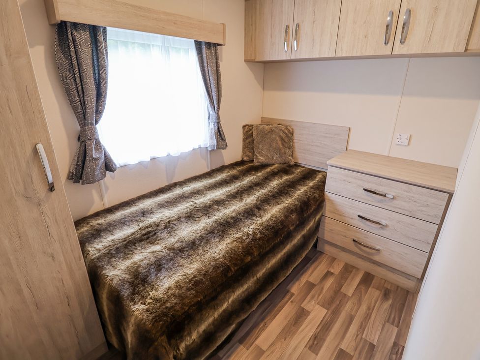 A bedroom with a bed covered in a fur blanket next to a window and a chest of drawers at The Hoot in Great Finborough near Stowmarket