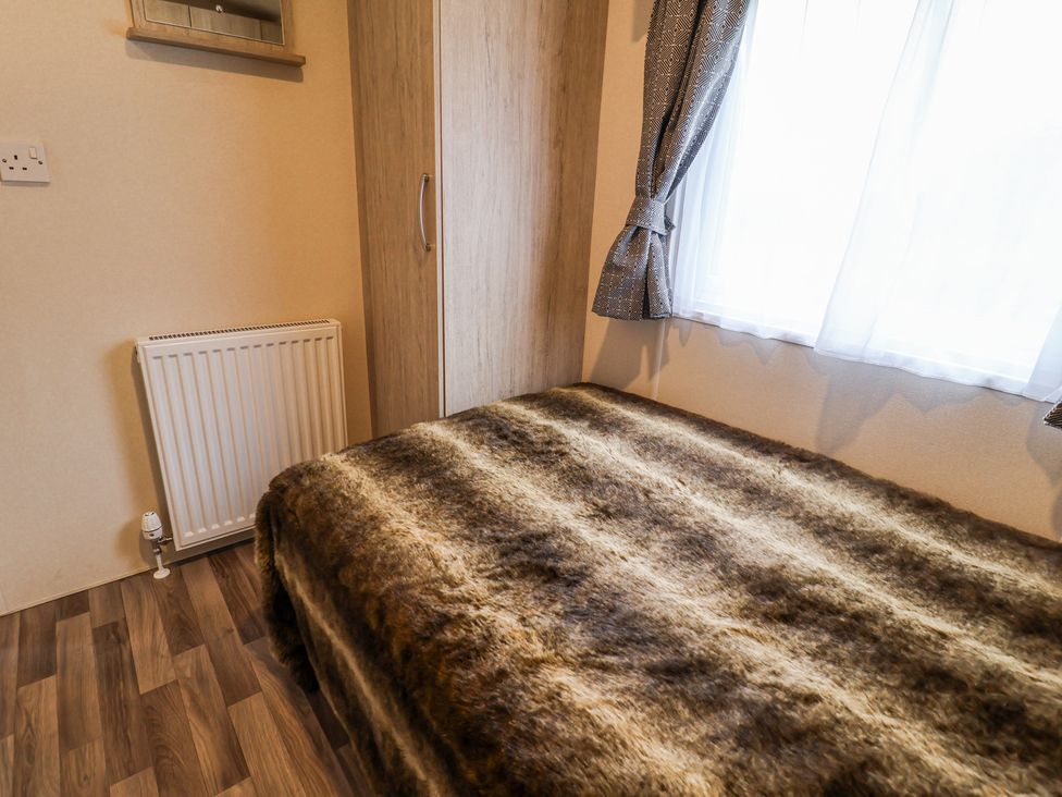 A bedroom with a bed covered with a brown furry blanket a wooden wardrobe a window with curtains and a radiator on the wall at The Hoot in Great Finborough near Stowmarket