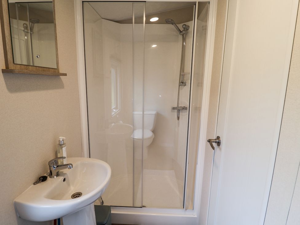 A bathroom with a pedestal sink soap dispenser mirrored cabinet shower enclosure and toilet reflected in the shower door at The Hoot in Great Finborough near Stowmarket