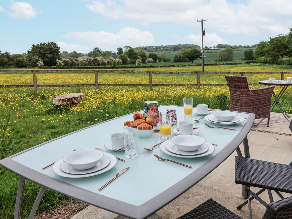 An outdoor dining table set with plates cups croissants and glasses of juice overlooking a field of yellow flowers at The Hoot in Great Finborough near Stowmarket