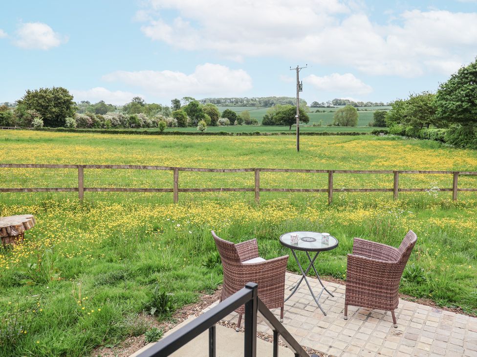 A patio with two chairs and a table overlooking a field with yellow flowers and trees at The Hoot in Great Finborough near Stowmarket