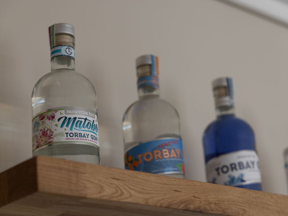Three bottles of Torbay gin on a wooden shelf at Lodge 65 at Riviera Bay Coastal Retreat Brixham