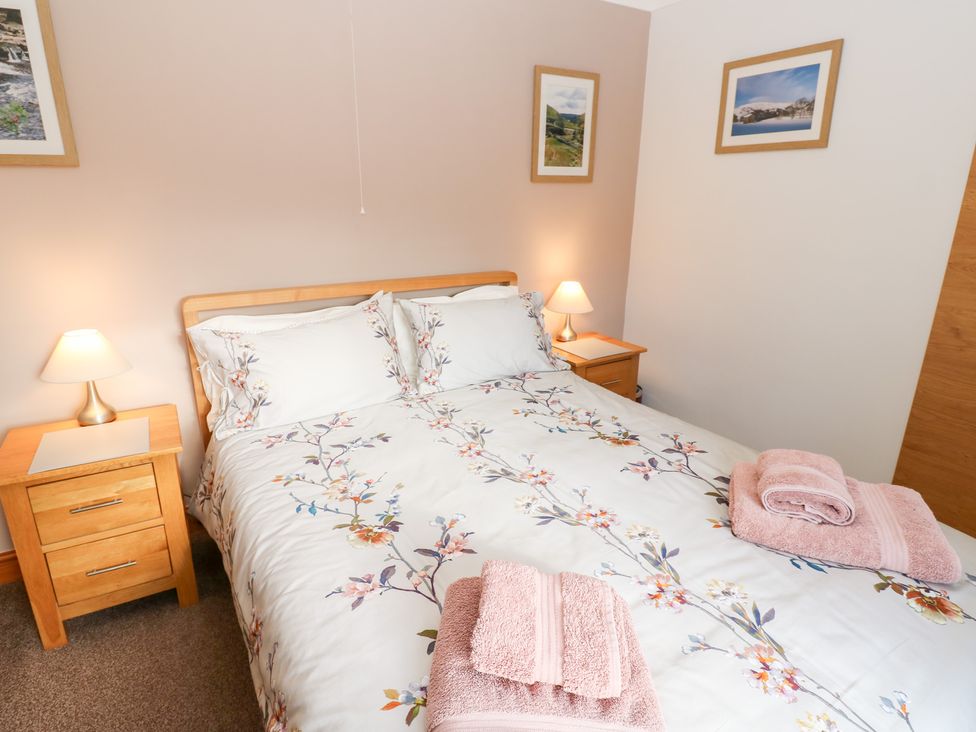 A bedroom with a bed, bedside tables, and framed pictures at Stoneleigh Cottage in Muker