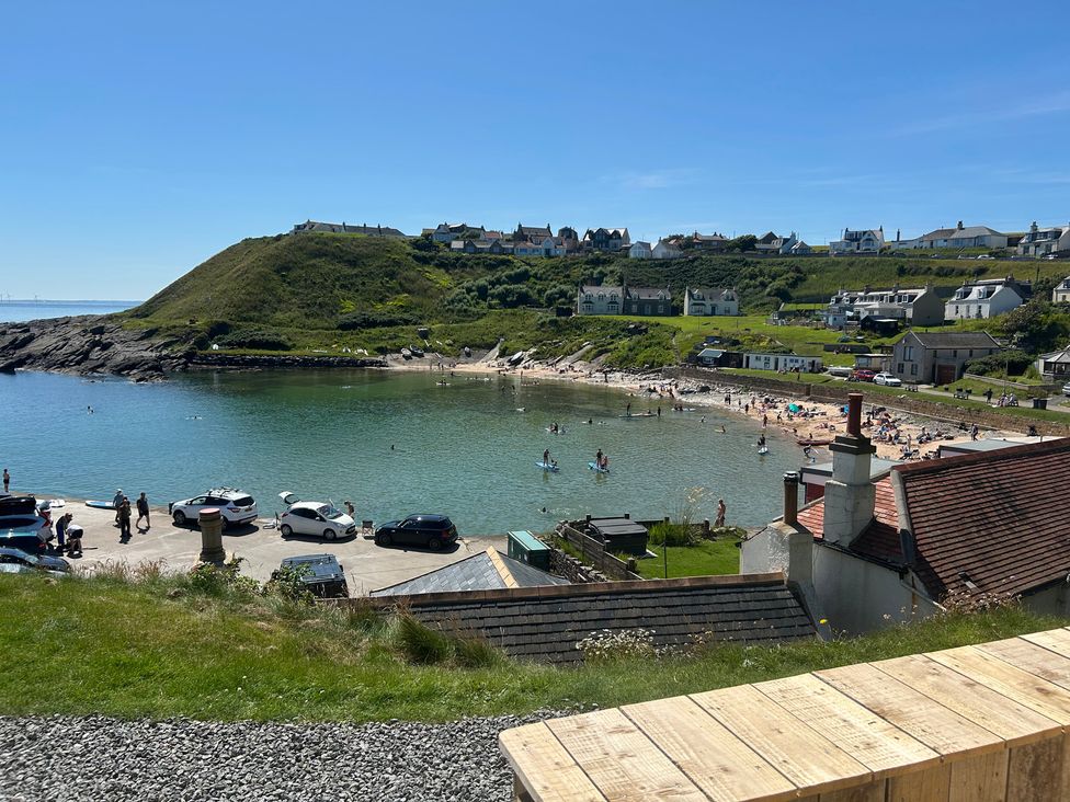 A beach with people in the water and houses on a hill at The Breakers in Newburgh, Aberdeenshire