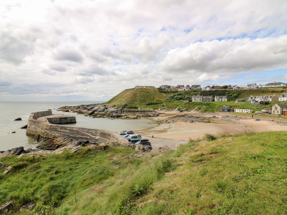 A beach with a pier and houses in the background at The Breakers in Newburgh, Aberdeenshire