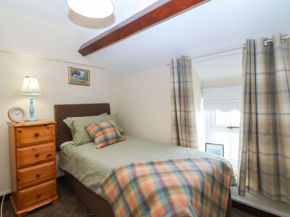 A bedroom with a bed, nightstand, lamp and window at Pant in Niwbwrch (newborough)