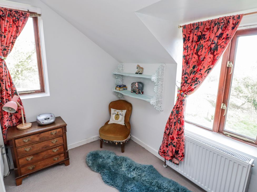 A bedroom corner with a chair, bookshelf, and window at Pencestyll in Cardigan