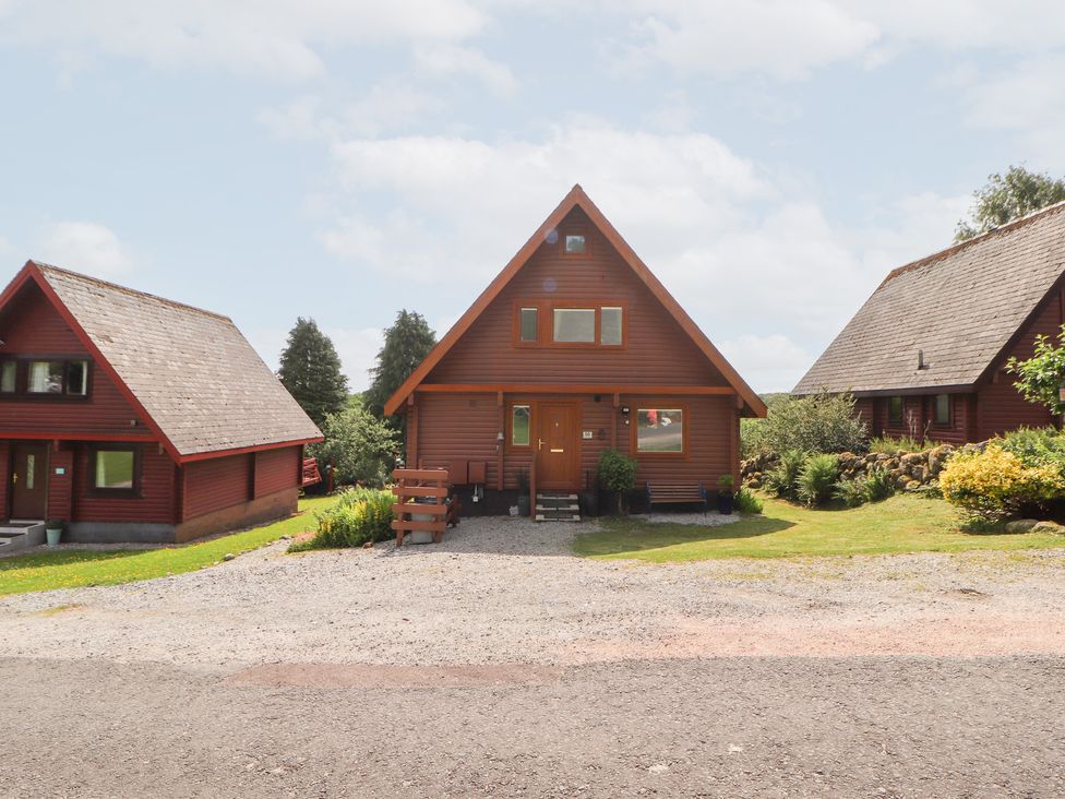 A log cabin with a front door and garden at Thistle Dubh ('Doo') in Sandyhills