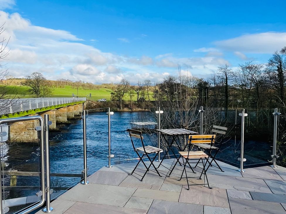 An outdoor seating area with a table and chairs near a river at Bridge End Cottage in Wark