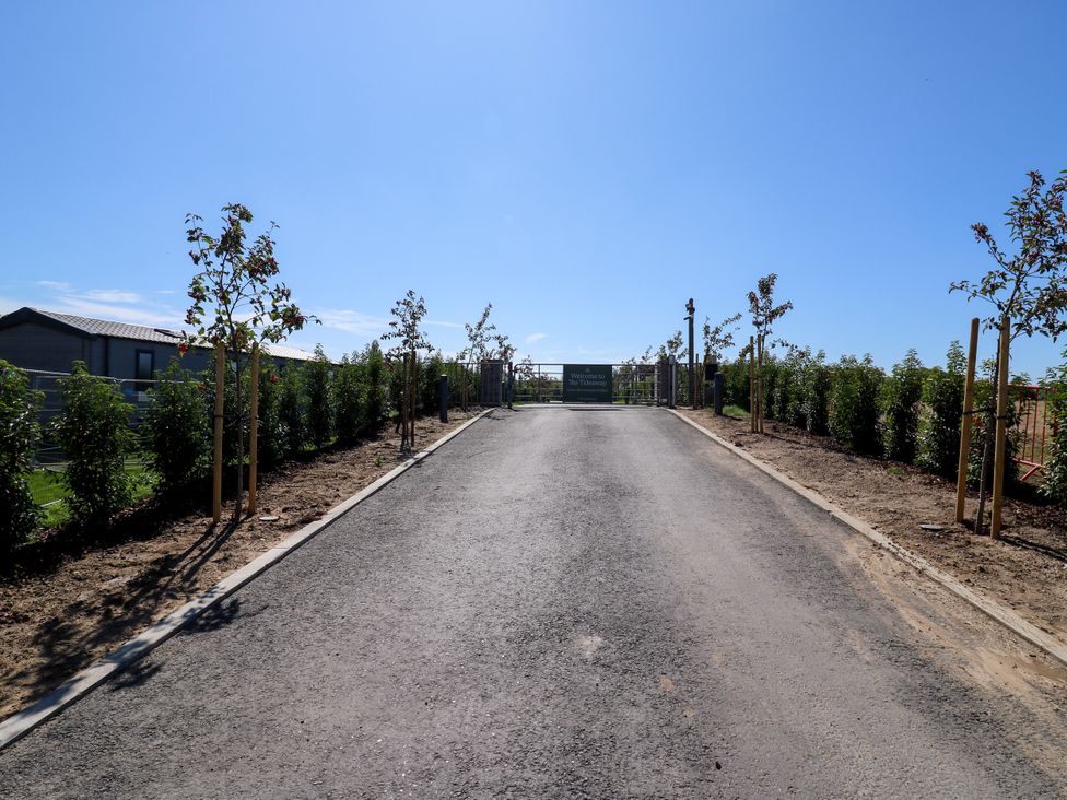 A roadway leading to a gate with trees lining the sides at The Farmhouse in St. Osyth