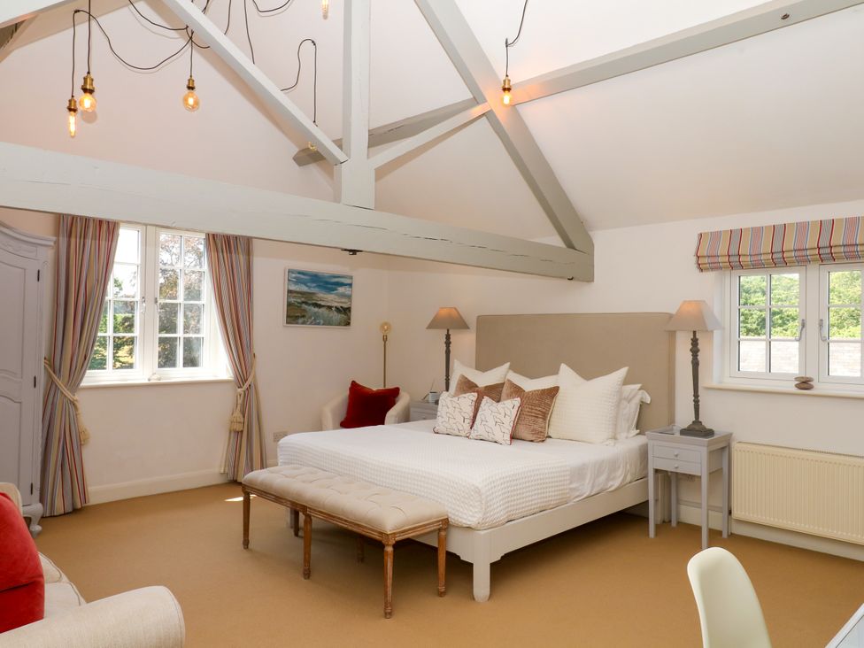 A bedroom with a bed, bench, lamps and windows at Apple Mill Venn Ottery near Sidmouth