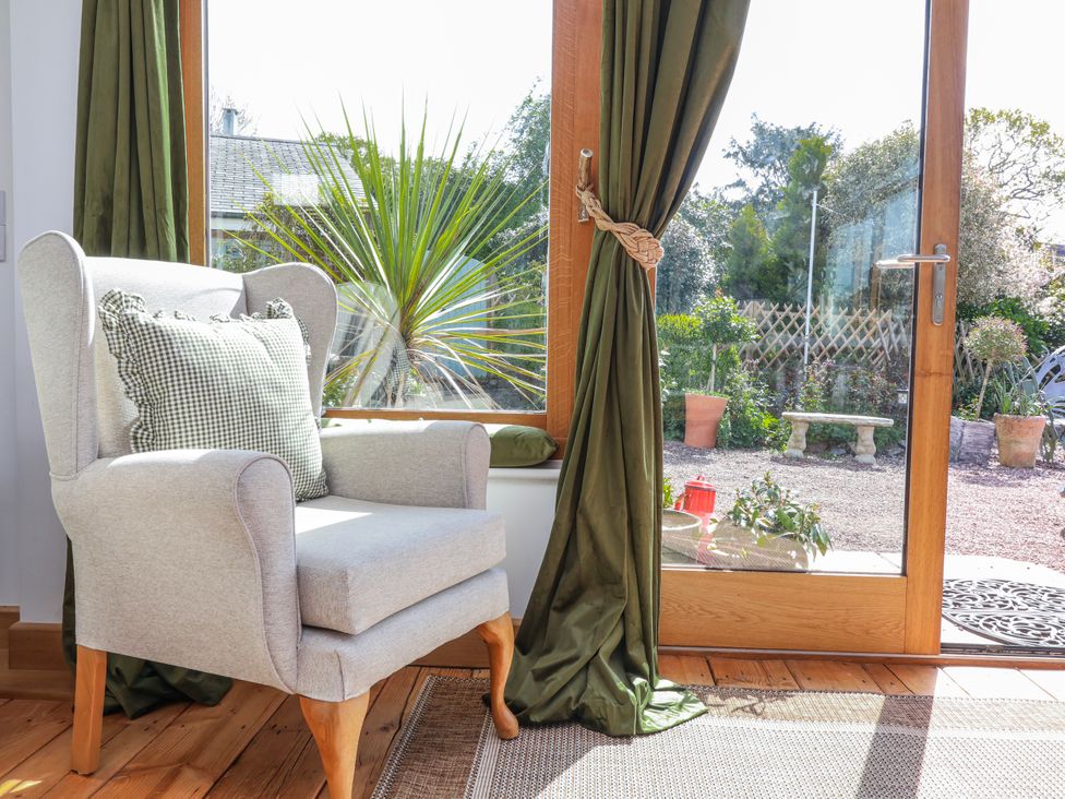 A conservatory with an armchair and a view of a garden at Burlodge in Swimbridge near Barnstaple