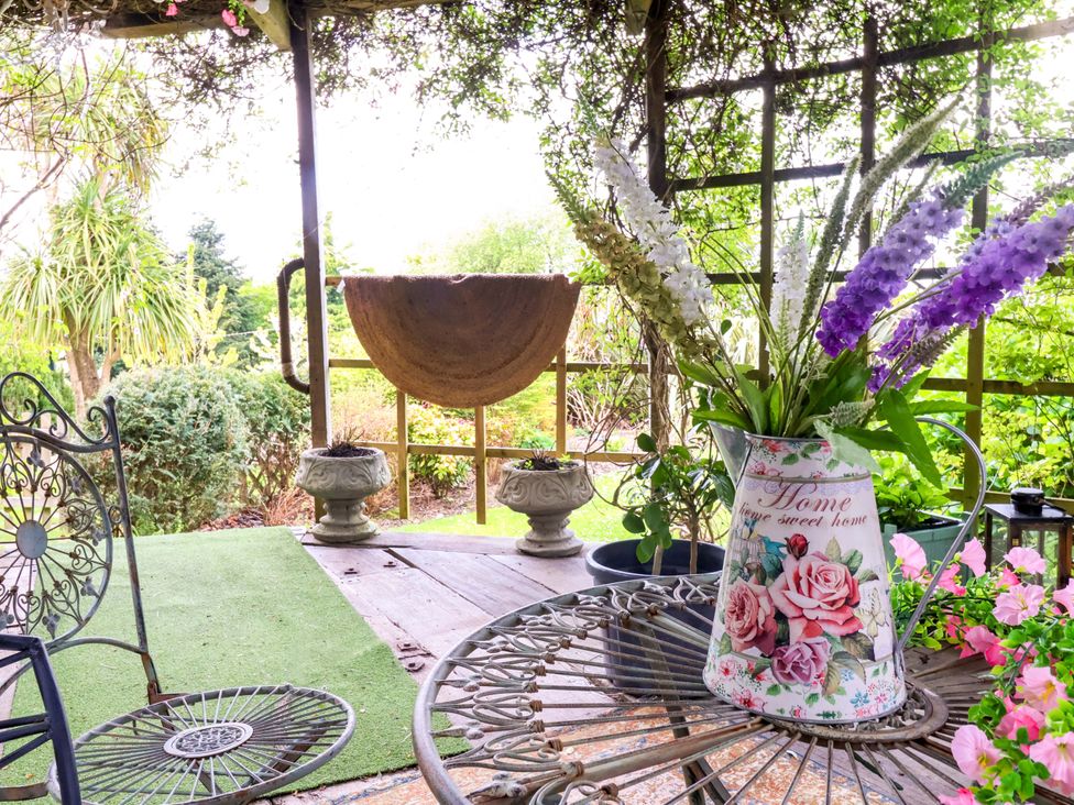 A garden with a table and flowers in a pitcher at Sunset Cottage in Swimbridge near Barnstaple