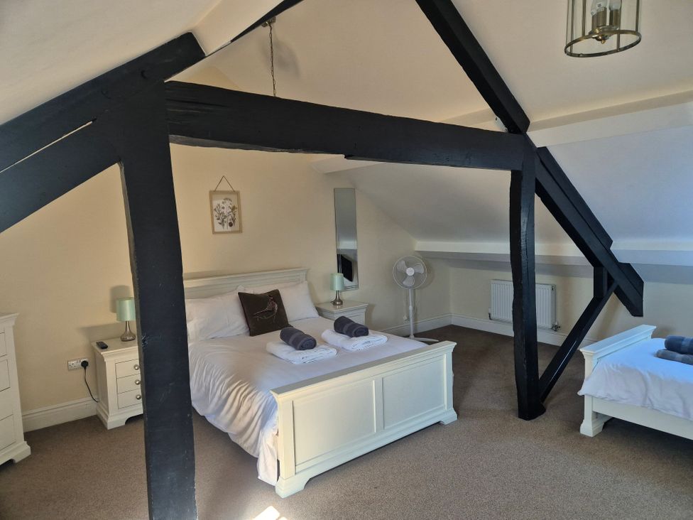 A bedroom with two white beds black wooden beams a standing fan and bedside tables at 12 Eagle Parade in Buxton
