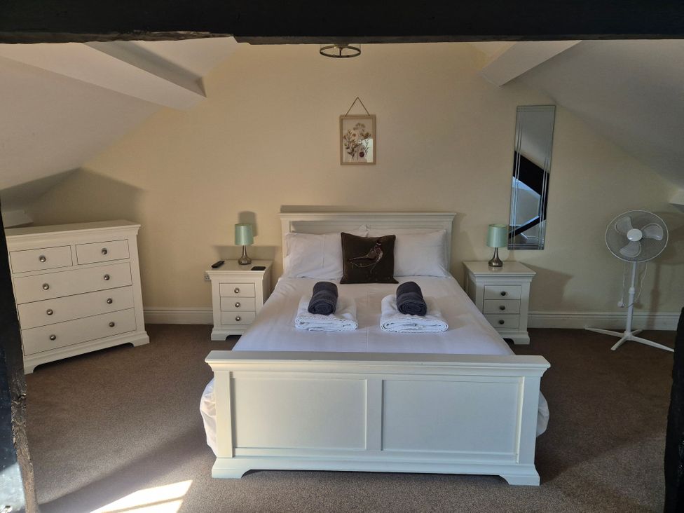 A bedroom with a white bed and bedside tables with lamps a chest of drawers a fan and a mirror at 12 Eagle Parade in Buxton