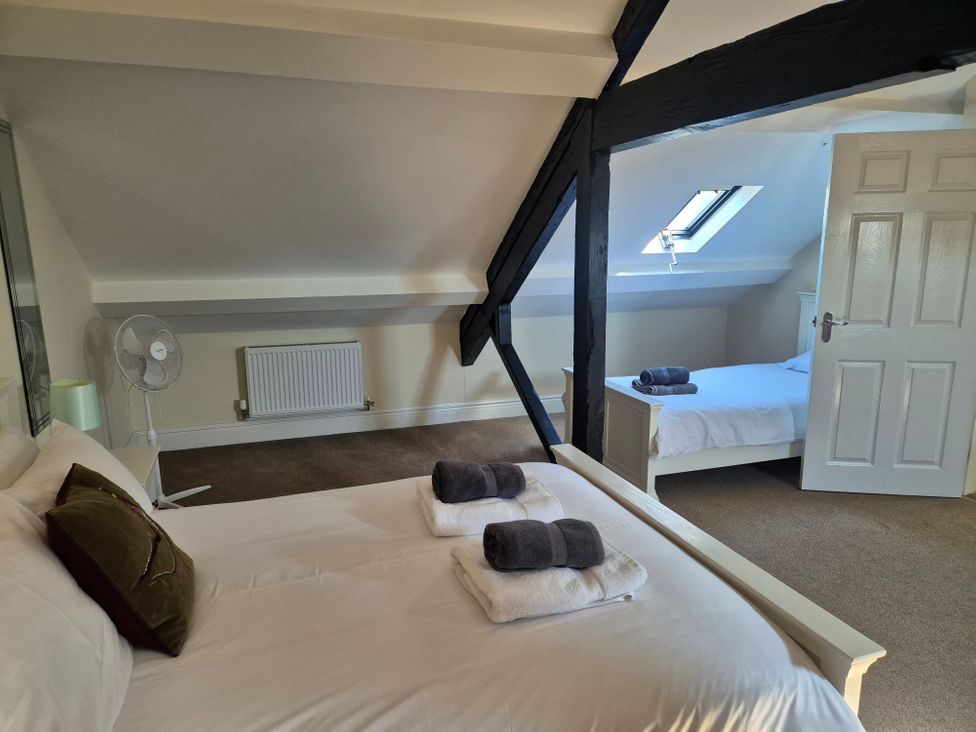 A bedroom with white beds and folded towels on them under slanted ceilings and wooden beams at 12 Eagle Parade in Buxton