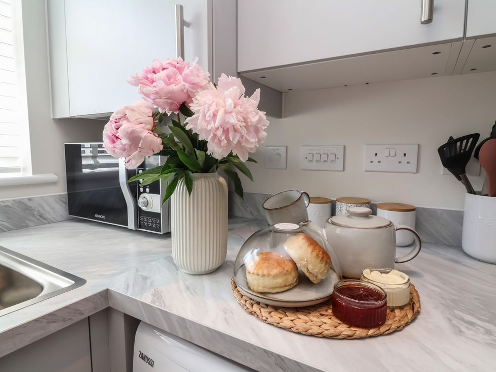 A kitchen counter with flowers, a microwave, scones, and a teapot at Seashell Sands in Appledore