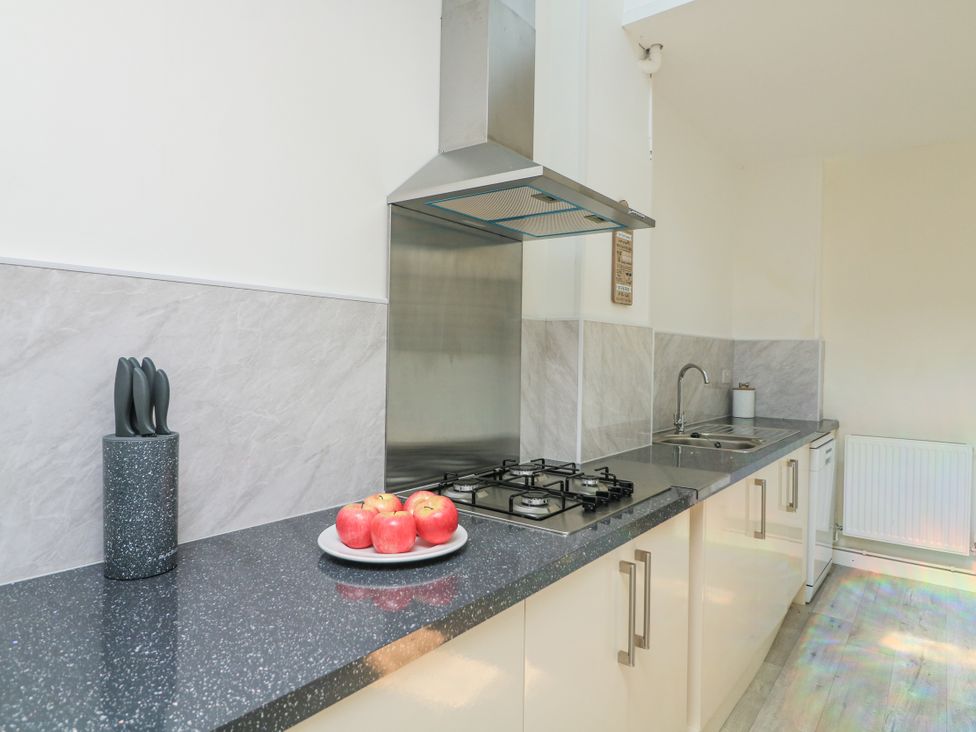 A kitchen with a stove, sink, and apples on the counter at Hougoumont Cottage in Torpoint