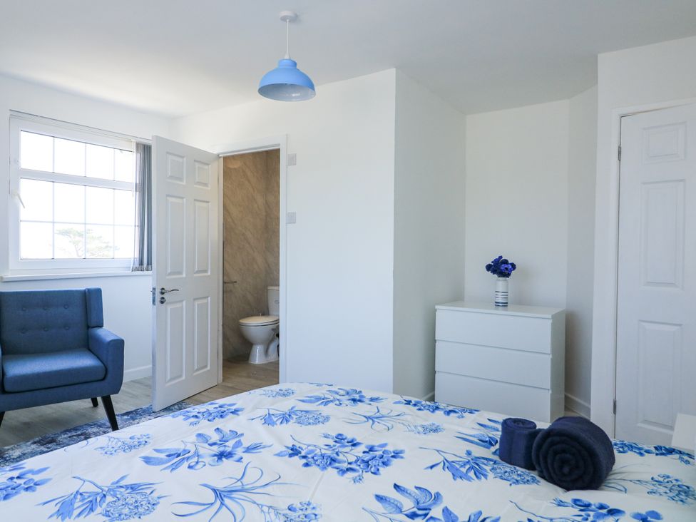 A bedroom with a chair and a door leading to a bathroom at Hougoumont Cottage in Torpoint
