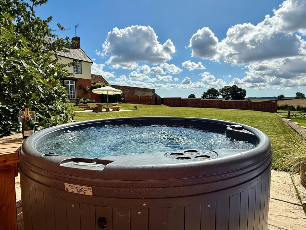A hot tub with a wine bottle and glass in the garden at Knights Farm in Harkstead