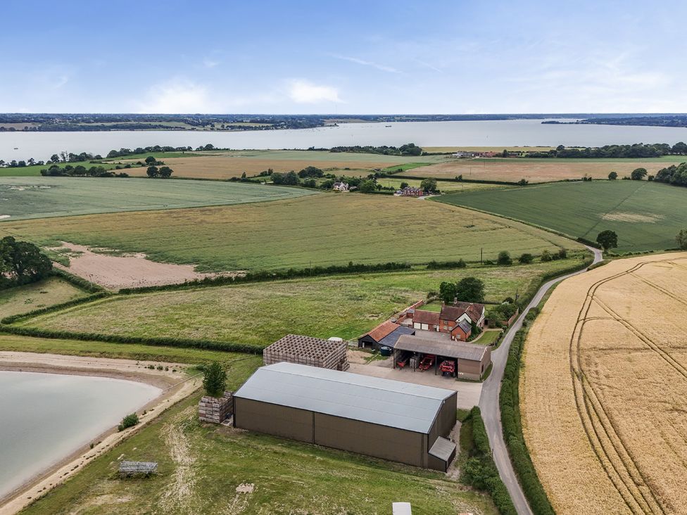 An aerial view of a farm with fields and a lake at Knights Farm Harkstead