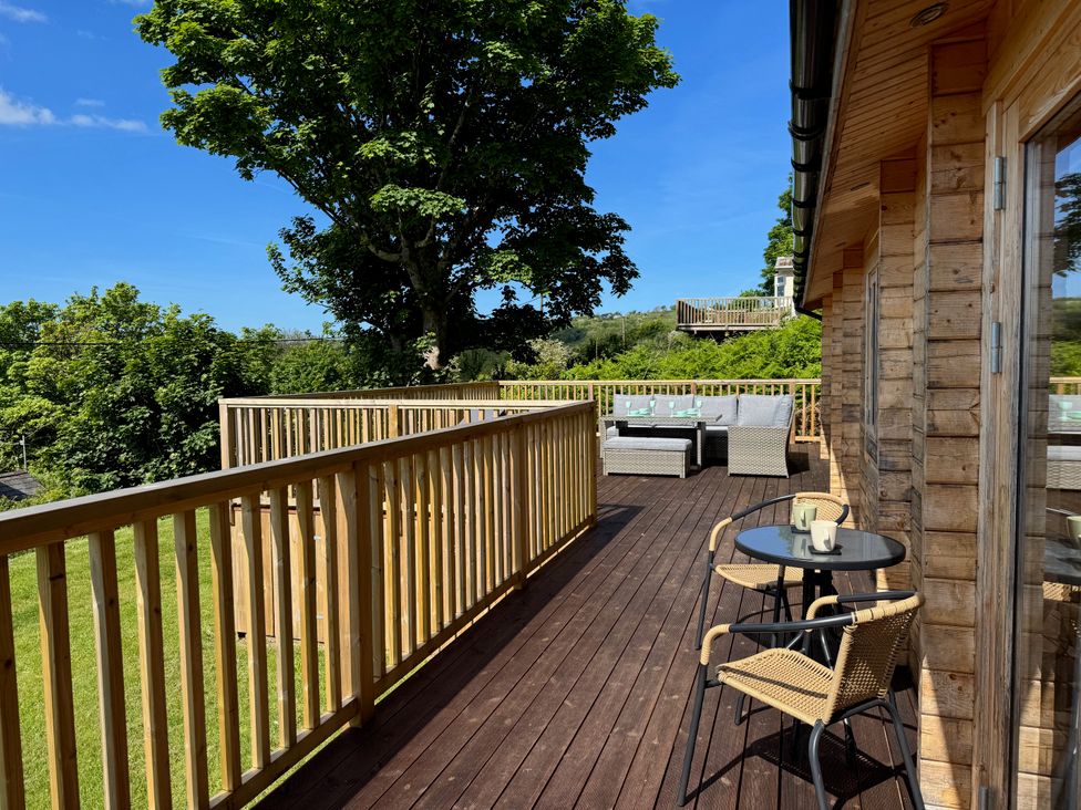 A wooden deck with outdoor seating and a table with two chairs at Northwood Lodge in Llanbedrog